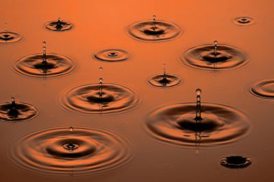Raindrops landing in a red-brown puddle